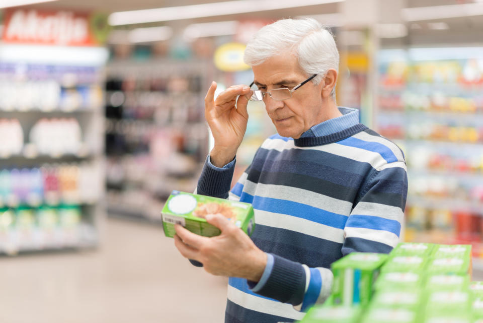 Older man holding an item at a supermarket and adjusting glasses to see it better