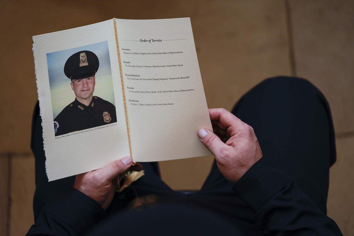 A U.S. Capitol Police Officer holds a program during a ceremony memorializing Officer Brian Sicknick, as an urn with his cremated remains lies in honor on a black-draped table at the center of the Capitol Rotunda, Wednesday, Feb. 3, 2021, in Washington.  (Demetrius Freeman/The Washington Post via AP, Pool)