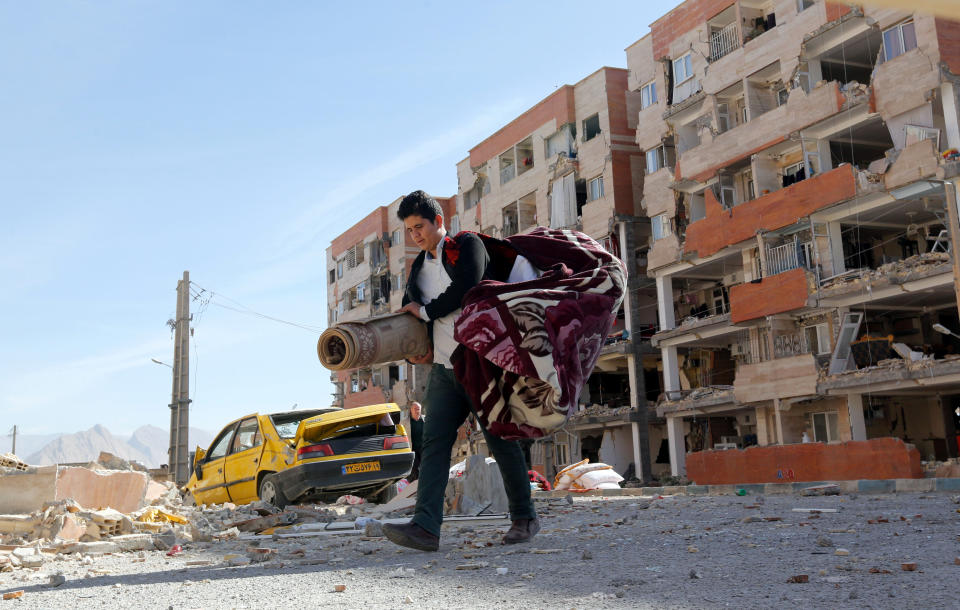 <p>An Iranian victim of the earthquake carries belongings near damaged buildings in the city of Pole-Zahab in Kermanshah Province, Iran, 13 Nov. 13, 2017. (Photo: Abedin Taherkenareh/EPA-EFE/REX/Shutterstock) </p>