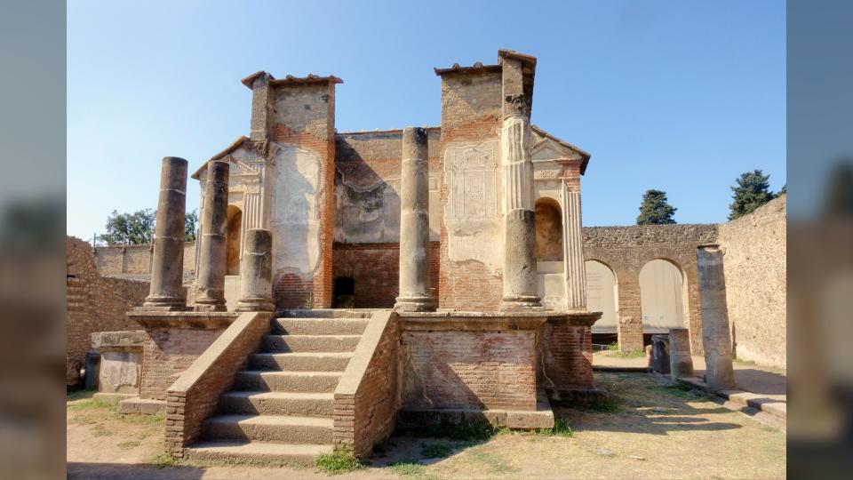 Here we see the ruins of the Temple of Isis mostly destroyed during the eruption of the volcano Vesuvius. There are stairs leading to a platform with several pillars and walls.