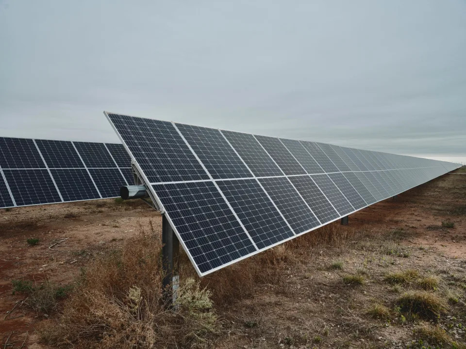 Rows of solar panels in a field against a cloudy sky.