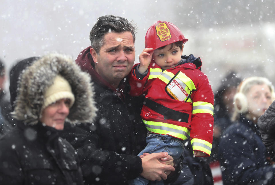 Mike Sullivan and his son, James Sullivan, 3, watch the funeral procession for fallen Buffalo Firefighter Jason Arno at the entrance to Forest Lawn Cemetery in Buffalo, N.Y., on Friday, March 10, 2023. The 37-year-old father who had been with the department for three years was killed in an explosive blaze. (Joseph Cooke/The Buffalo News via AP)