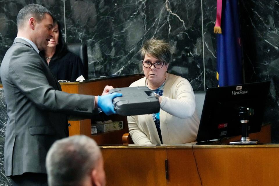 Gun shop office manager Cammy Back looks over the gun case held Friday by Oakland County Assistant Prosecutor Marc Keast. The case went with a handgun sold to James Crumbley on Black Friday 2021.