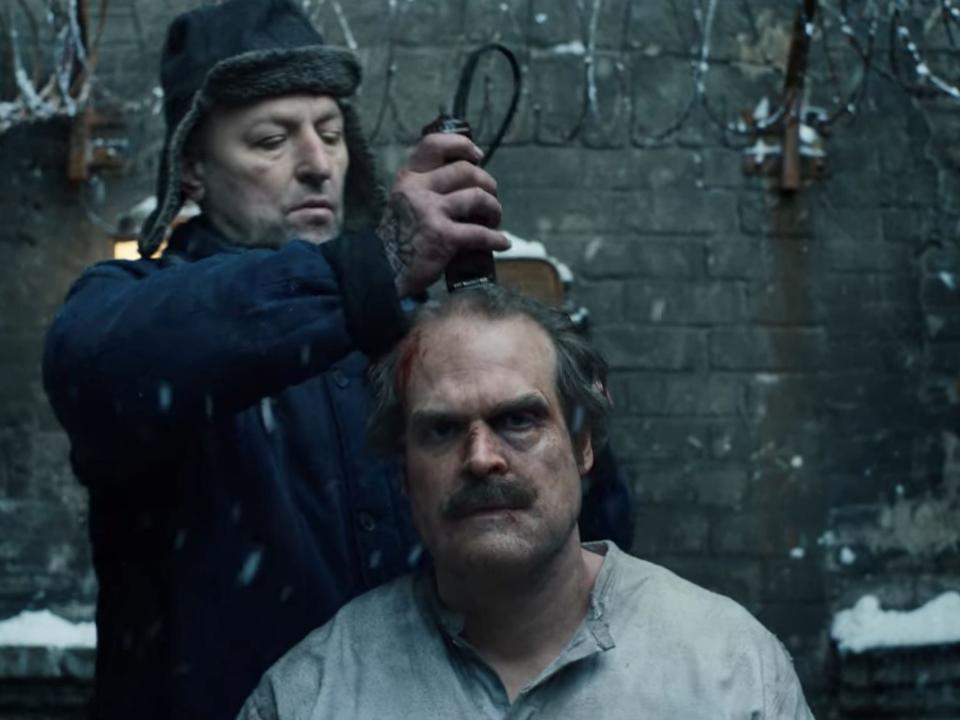 A middle-aged man having his head shaved by a prison guard.