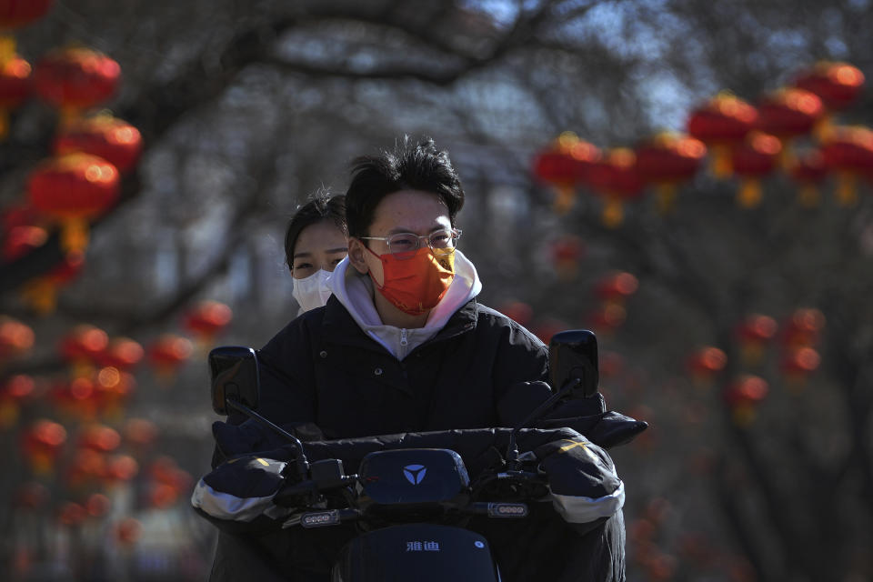 Residents wearing face masks to help protect from the coronavirus ride an electric scooter along a street decorated with red lanterns in Beijing, Tuesday, Feb. 8, 2022. China has ordered inhabitants of the southern city of Baise to stay home and suspended transportation links amid a surge in COVID-19 cases at least partly linked to the omicron variant. (AP Photo/Andy Wong)