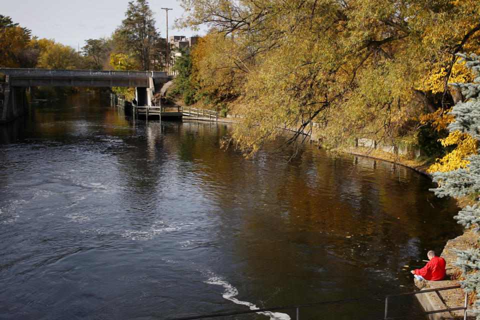 FILE - This Nov. 3, 2011, file photo shows a fisherman sitting near the Boardman River dam in Traverse City, Mich. The Boardman River, which meanders through town before flowing into the lake. Boardwalks and parks adjoin sections of the river, where you can watch anglers land brook trout or ducks peck for food in the shallows. A few blocks south of downtown, the river widens into Boardman Lake, with a 2-mile-long paved and dirt trail. (AP Photo/Traverse City Record-Eagle, Keith King)