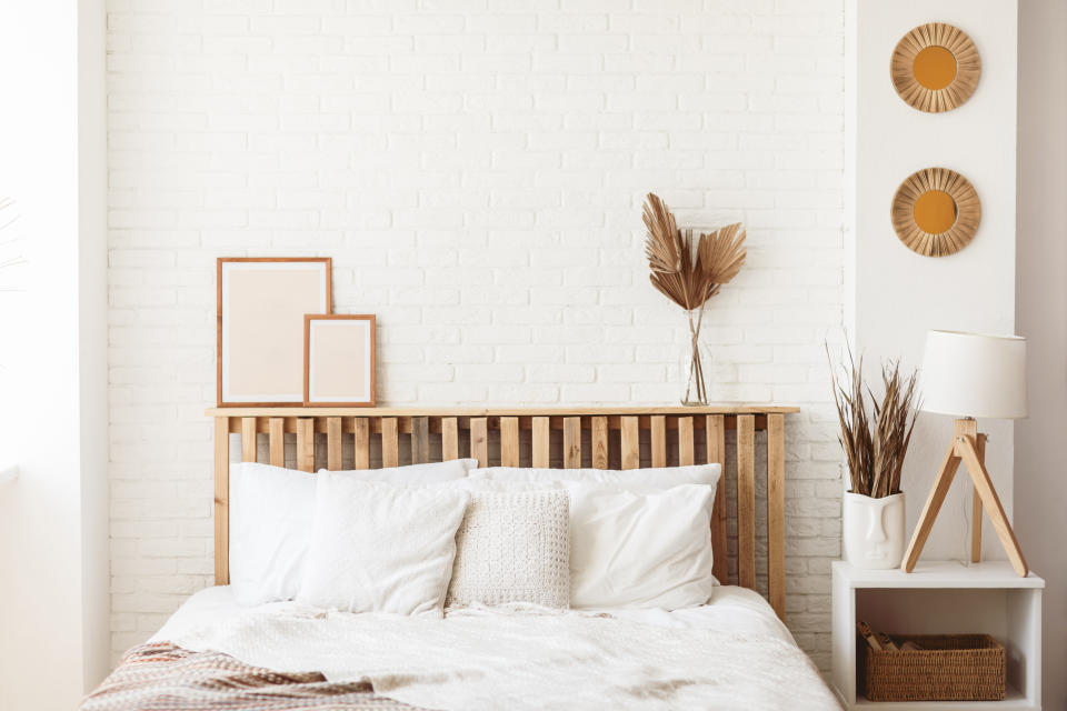 Wooden headboard with dry gold palm leaves in a glass vase and two photo frames on it. Stylish trendy decoration with copy space.