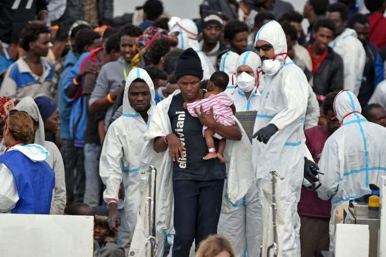 A woman carries her baby as she disembarks from the Italian Coast Guard vessel "Diciotti" which landed hundreds of refugees rescued in the Mediterranean