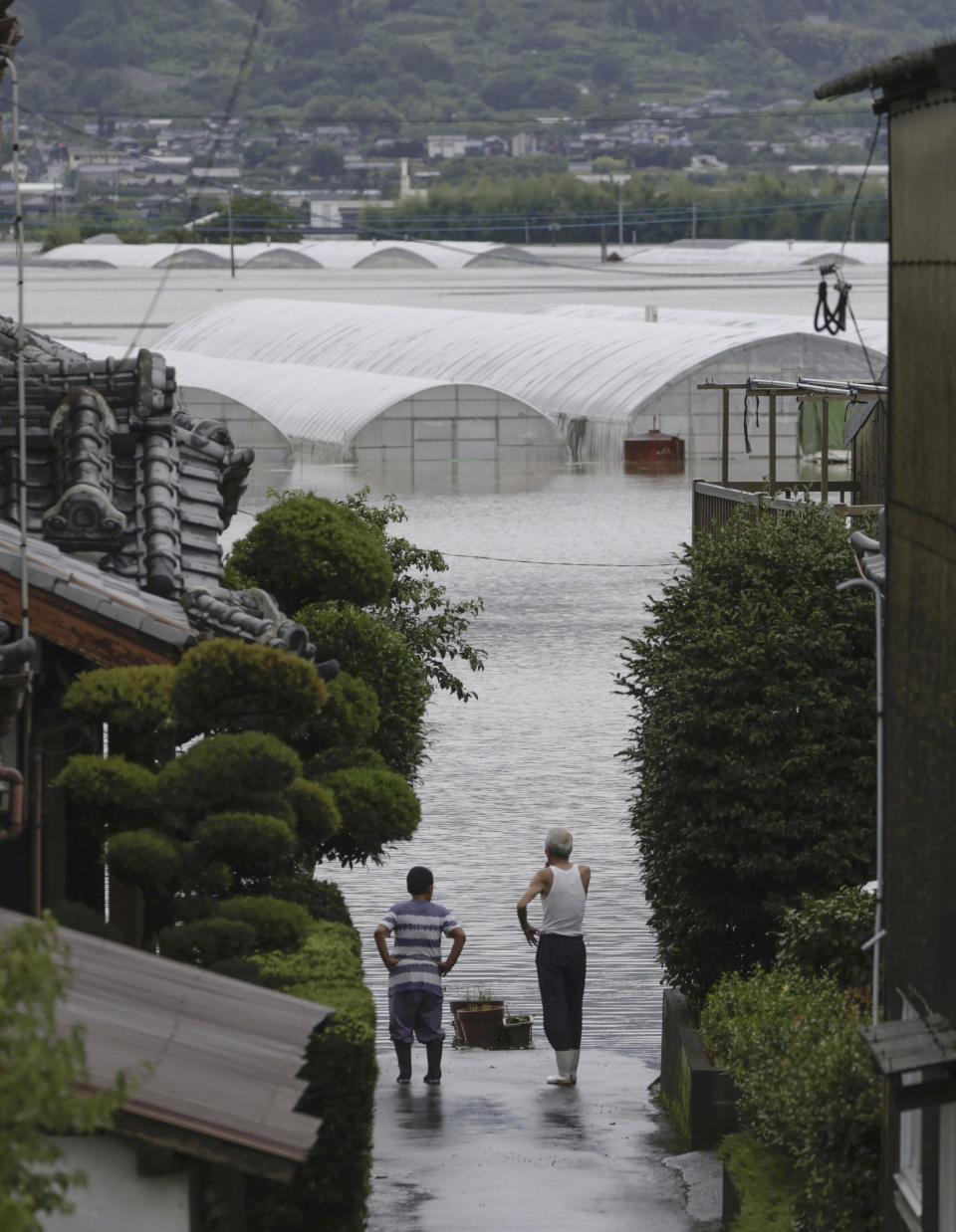 People stand near a flooded area due to a heavy rain in Kurume, Fukuoka prefecture, southern Japan Monday, July 10, 2023. Torrential rain has been pounding southwestern Japan, triggering floods and mudslides. (Kyodo News via AP)