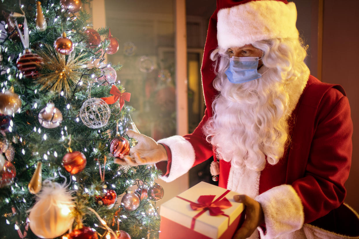 Santa Claus with a protective mask on his face during New Year's Eve brings a Christmas gift for children. He wears his red suit and Santa's hat, but also a protective face mask during the corona virus outbreak