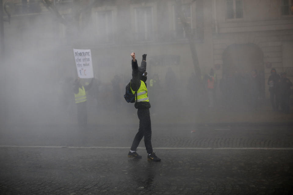 A demonstrators raises his arms amid tear gas during a yellow vest protest Saturday, Jan. 19, 2019 in Paris. Thousands of yellow vest protesters rallied Saturday in several French cities for a 10th consecutive weekend, despite a national debate launched this week by President Emmanuel Macron aimed at assuaging their anger. (AP Photo/Thibault Camus)