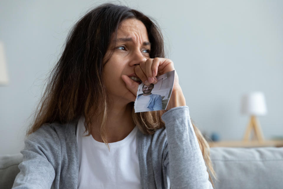 Close up crying woman holding torn picture of ex. (Getty Images)