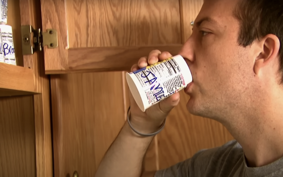 Person drinking from a small carton with a cabinet door open behind them