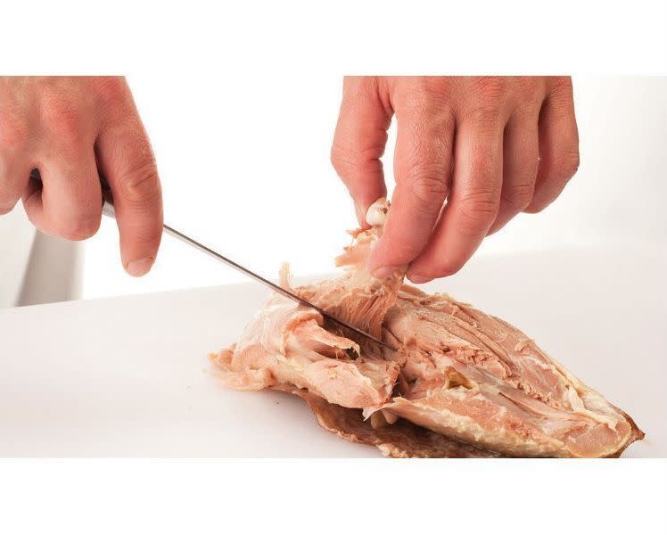 Hold the knife blade parallel to the board and slip it underneath the bone. Cut along the length of the bone to free it from the meat. Pull the bone away from the meat.