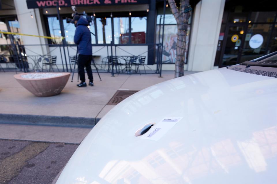 An evidence marker is placed next to a bullet hole in the hood of a Honda Civic parked along the curb near a pizza parlor on Dec. 28, 2021 in Lakewood, Colo., one of the scenes of a shooting spree that left five people dead—including the suspected shooter.