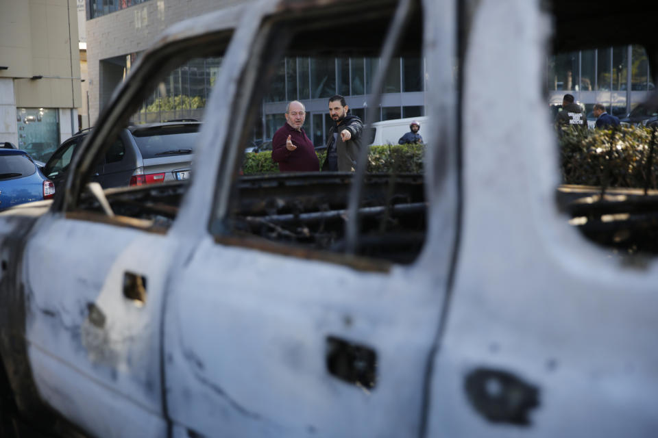 People look at a burned car that was set on fire early Tuesday by supporters of the Shiite Hezbollah and Amal Movement groups, in Beirut, Lebanon, Tuesday, Dec. 17, 2019. Supporters of Lebanon's two main Shiite groups Hezbollah and Amal clashed with security forces and set fires to cars in the capital early Tuesday, apparently angered by a video circulating online that showed a man insulting Shiite figures.(AP Photo/Hussein Malla)