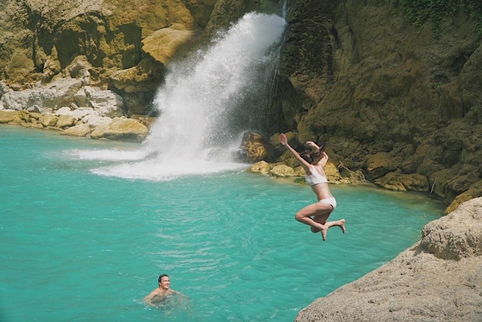 A woman jumping into a body of water where a man is waiting.