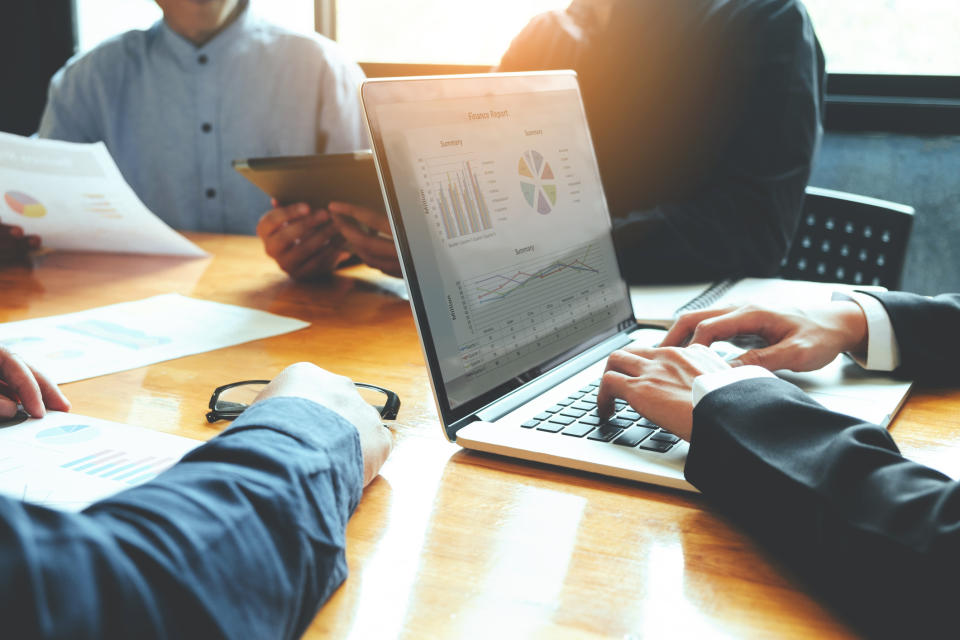 Several people work at a conference table, referring to financial charts.