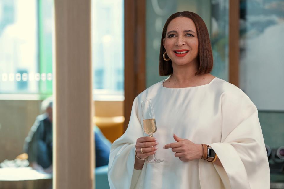 Maya Rudolph in an elegant white dress with a champagne glass in her hand, smiling at an event