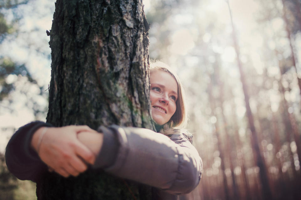 Woman hugging tree in the forest with sunlight in the background.