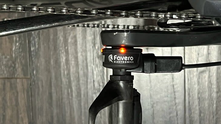 A magnetic clip holds the charging connector in place. LEDs indicate charging status of the Favero Assioma Shi power meter.