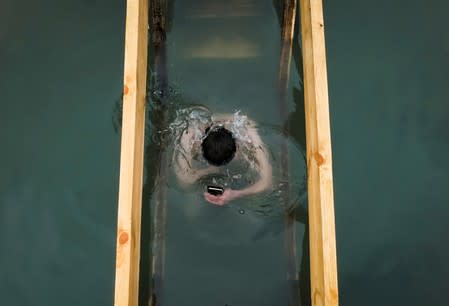 FILE PHOTO: A man holds his smartphone as he takes a dip during Epiphany celebration at the Bolshaya Almatinka river bank in Almaty