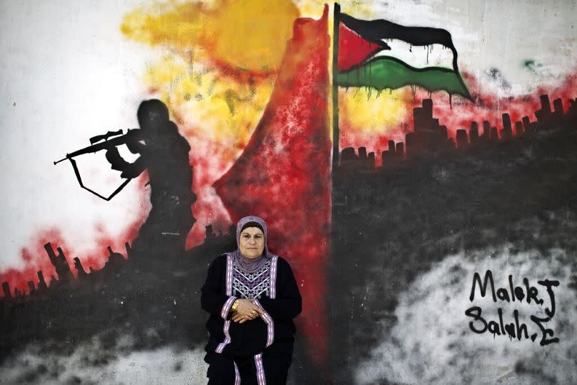 La réfugiée palestinienne Layla Afaneh, 67 ans, pose pour une photo devant un mur peint avec une peinture murale dans le camp de réfugiés de Kalandia, 2014