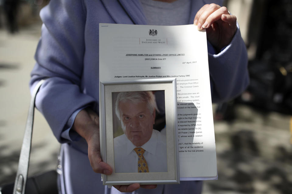 Karen Wilson, widow of postmaster Julian Wilson who died in 2016, holds a photograph of her husband outside the Royal Courts of Justice, London, after his conviction was overturned by the Court of Appeal, Friday, April 23, 2021. A British appeals court has overturned the convictions of 39 postmasters and postmistresses who were accused of theft, fraud and false accounting following the installation of a new computer system in local branches. Announcing the Court of Appeal ruling on Friday, a judge said Britain’s postal service “knew there were serious issues about the reliability” of the Horizon computer system and had a “clear duty to investigate” its defects. (Yui Mok/PA via AP)