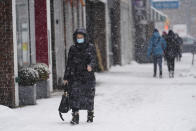 Pedestrians wear protective masks during the coronavirus pandemic as they walk along 71st Avenue as snow falls Thursday, Feb. 18, 2021, in the Queens borough of New York. (AP Photo/Frank Franklin II)