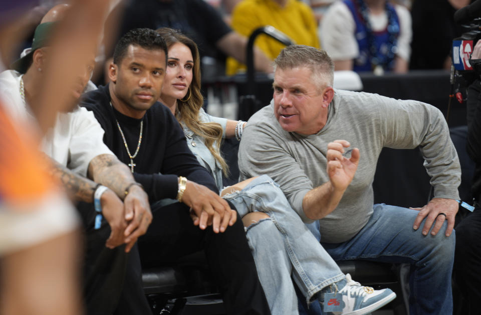 L'entraîneur-chef des Broncos de Denver, Sean Payton, à droite, discute avec le quart-arrière Russell Wilson, à gauche, tandis que l'épouse de Payton, Skylène, regarde depuis les sièges du terrain lors d'un match éliminatoire des Denver Nuggets.  (AP Photo/David Zalubowski)