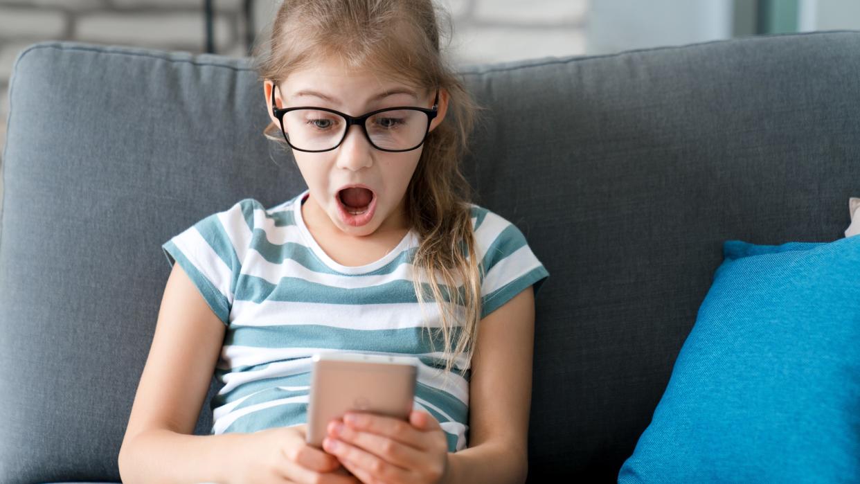  Child girl looking at mobile phone at home, with a surprised expression on her face 