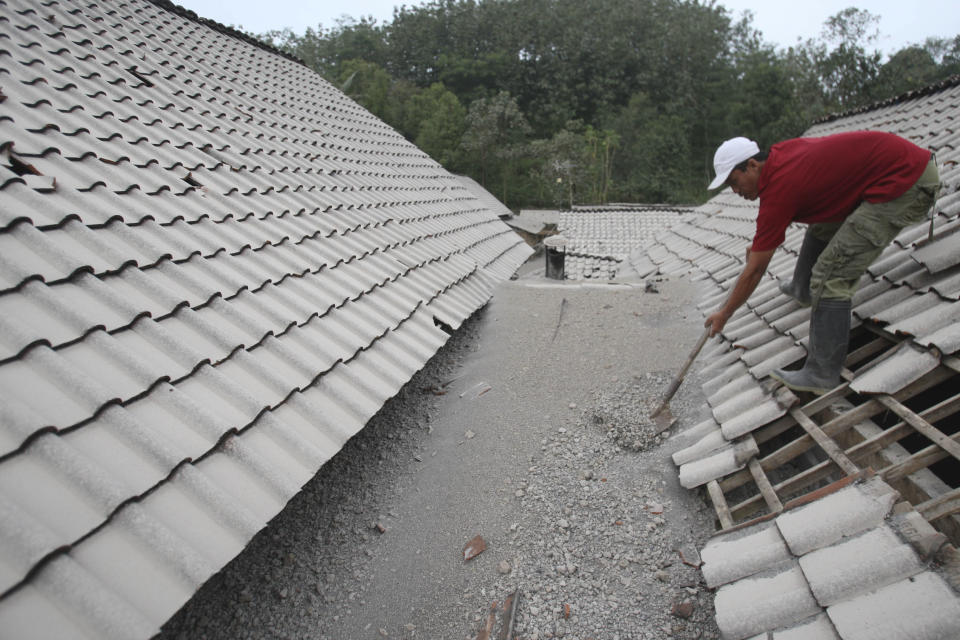 A man cleans a roof covered with volcanic ash from an eruption of Mount Kelud at Mbladak village in Blitar, Indonesia, Friday, Feb. 14, 2014. Volcanic ash from a major eruption in Indonesia shrouded a large swath of the country's most densely populated island on Friday, closed three international airports and sent thousands fleeing. (AP Photo/Trisnadi)