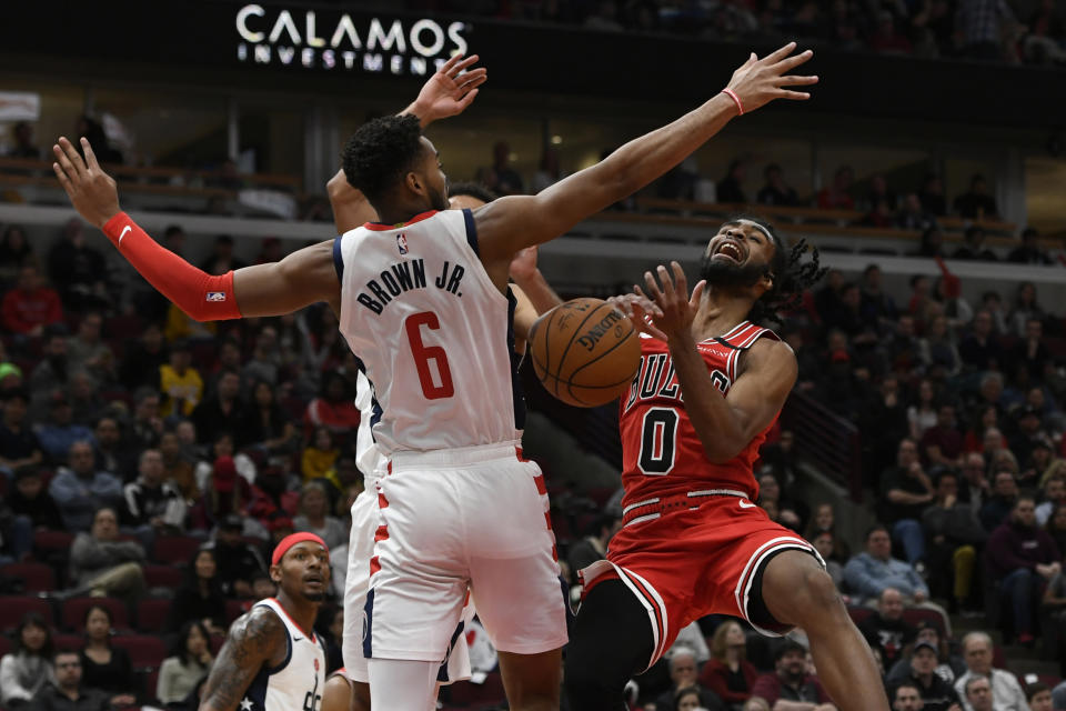 Chicago Bulls' Coby White (0) goes up for a shot against Washington Wizards' Troy Brown Jr. (6) and Jerome Robinson (12) during the second half of an NBA basketball game Sunday, Feb. 23, 2020, in Chicago. Chicago won 126-117. (AP Photo/Paul Beaty)