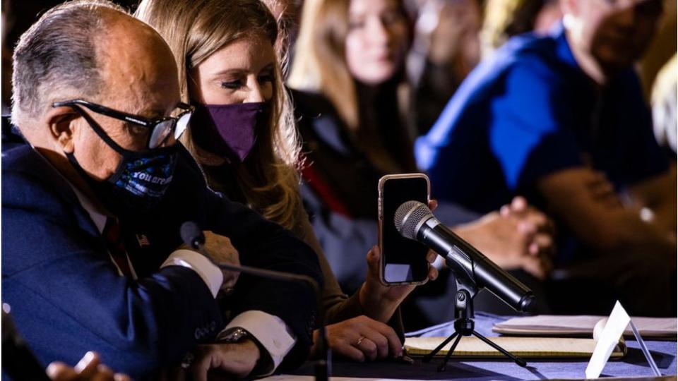 Rudy Giuliani y la abogada Jenna Ellis escuchan al presidente Trump por los parlantes de un teléfono móvil.