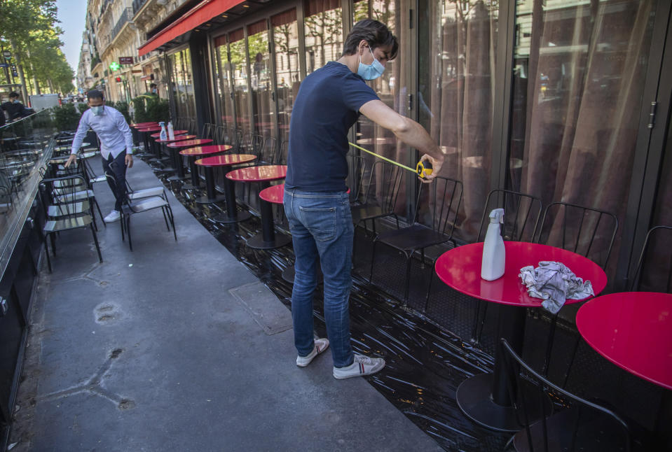 Pierre-Antoine Boureau con una cinta métrica instala las mesas en la terraza de un cadé en París, 1 de junio de 2020. (AP Foto/Michel Euler)