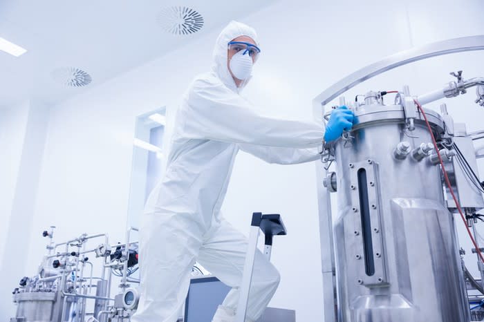 A technician servicing a stainless steel bioreactor used in drug manufacturing.