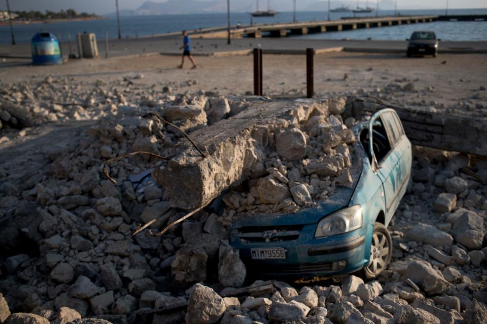 A man walks past a car crushed under rubble near the port of the Greek island of Kos - Credit: Petros Giannakouris/AP