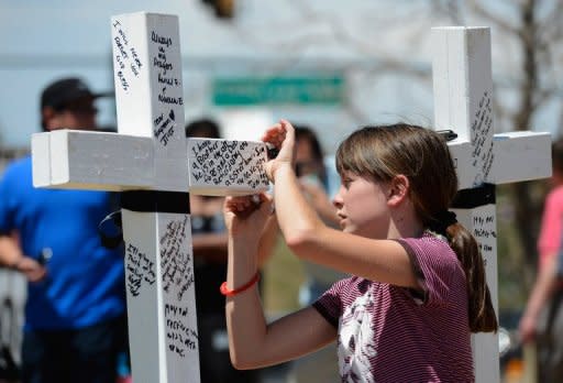 Emma Brazelton, 11, writes a personal note on a white wood cross with the name of each victim who was killed during the last weekend's mass shooting at Century 16 movie theater, in Aurora, Colorado