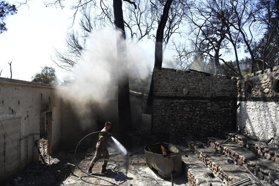 A firefighter operates at a burned house after a wildfire in Lampiri village, east of Patras city, Greece, Sunday, Aug. 1, 2021. A wildfire that broke out Saturday in western Greece forced the evacuation of four villages and people on a beach by the Fire Service, the Coast Guard and private boats, authorities said. (AP Photo/Andreas Alexopoulos)