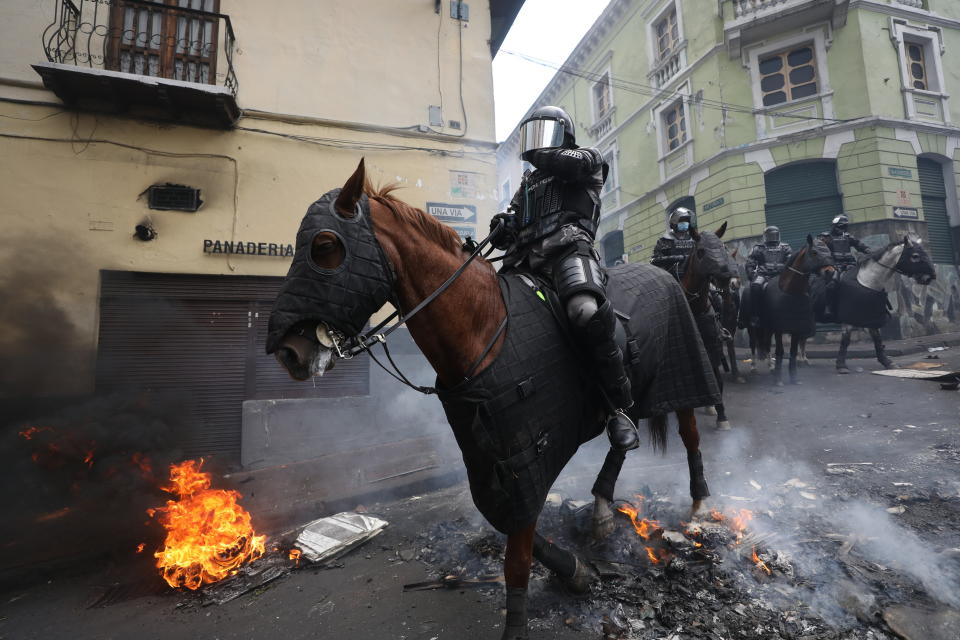 Mounted police cross a burning barricade in chase of anti-government demonstrators during a nationwide strike against President Lenin Moreno and his economic policies, in Quito, Ecuador, Wednesday, Oct. 9, 2019. Ecuador's military has warned people who plan to participate in a national strike over fuel price hikes to avoid acts of violence. The military says it will enforce the law during the planned strike Wednesday, following days of unrest that led Moreno to move government operations from Quito to the port of Guayaquil. (AP Photo/Fernando Vergara)