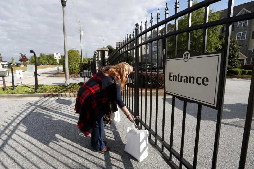 FILE - In this April 30, 2020 file photo, Crystal Craft places a bag of food at the gate for her husband, Justin, before sitting down for their weekly dinner date on opposite sides of a fence surrounding the Park Springs senior community, where Justin runs the food and beverage department in Stone Mountain, Ga. Workers who agreed to live at a Georgia nursing home to keep its residents safe from the coronavirus will embrace their loved ones for the first time in more than two months on Saturday, June 13 as the home lifts a shelter-in-place restriction on its staff. (AP Photo/John Bazemore, File)