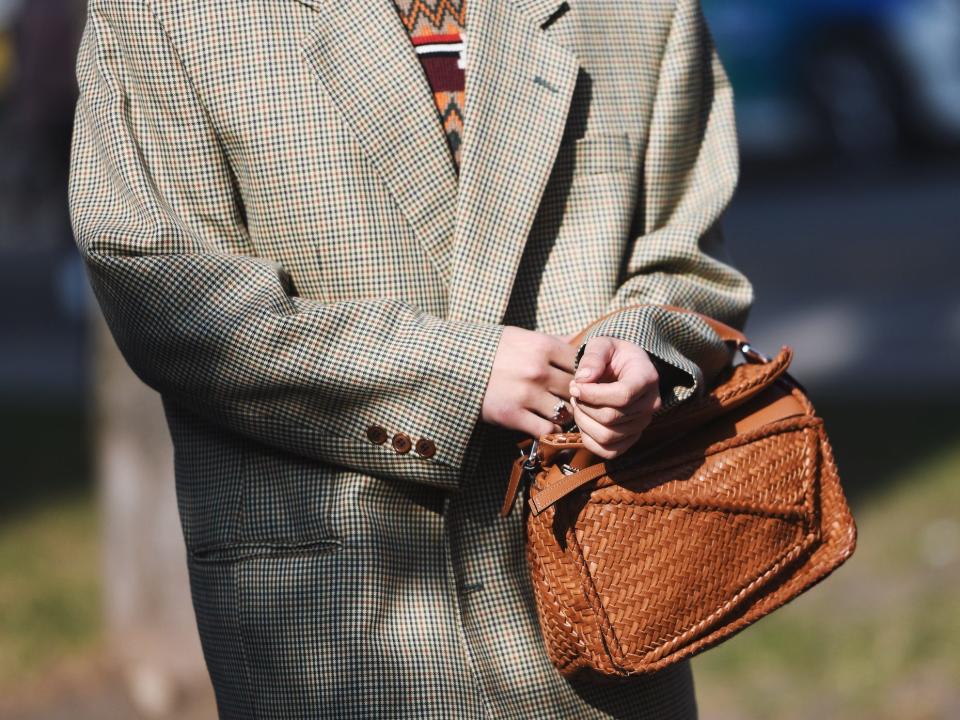 person wearing a sweater under an oversized tweed blazer and holding a woven purse