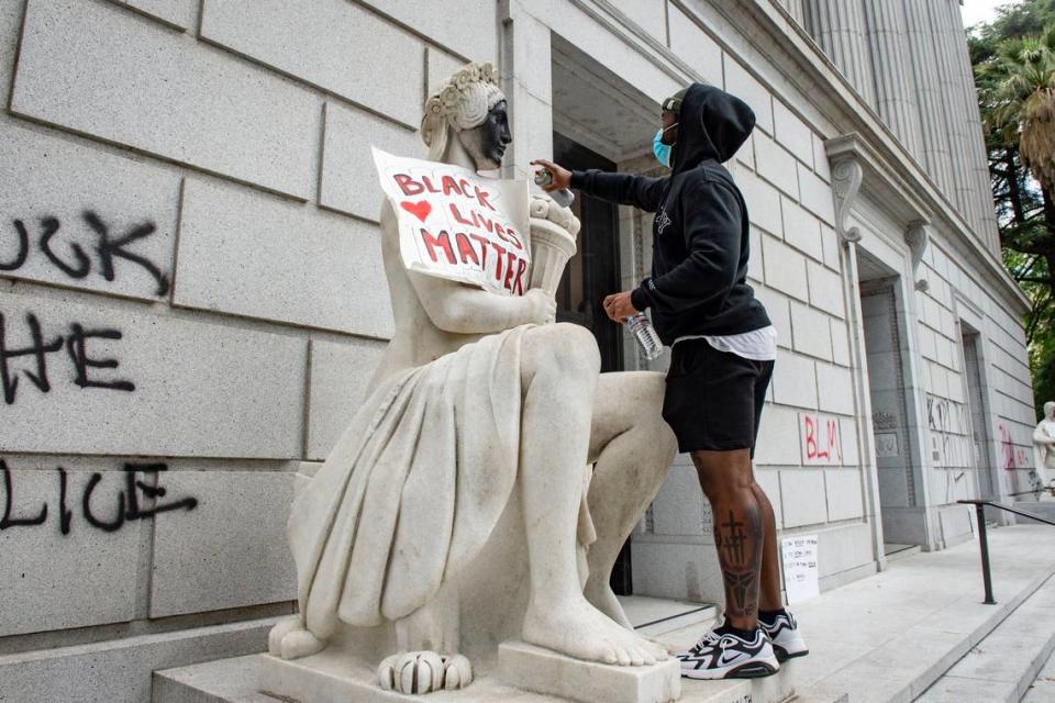 A protester spray paints a statue in front of the California State Library in downtown Sacramento on Saturday, May 30, 2020. Protests and riots have erupted around the country after the death of George Floyd at the hands of a police officer in Minneapolis, Minnesota.