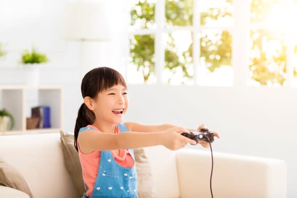 Laughing little girl playing video games on sofa.
