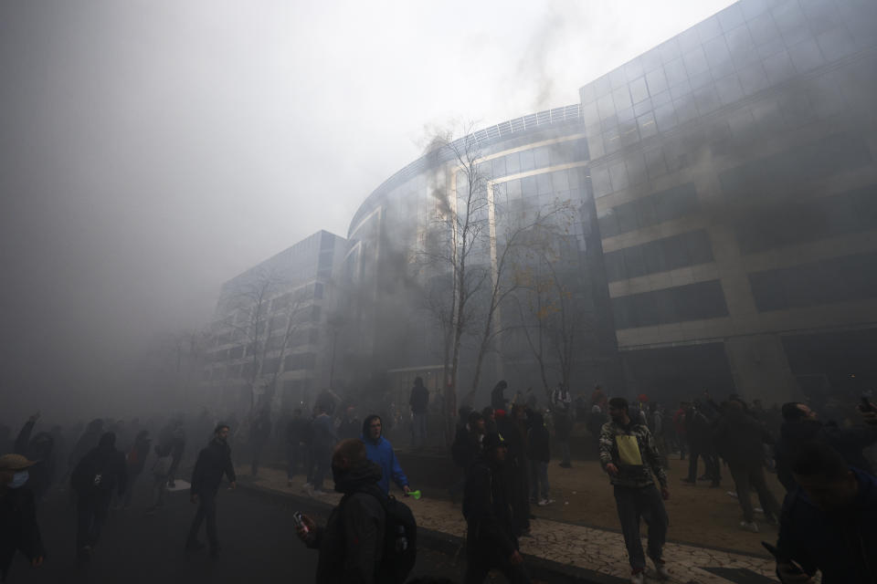 Protestors walks through smoke dust during a demonstration against the reinforced measures of the Belgium government to counter the latest spike of the coronavirus in Brussels, Belgium, Sunday, Nov. 21, 2021. Many among them also protested against the strong advice to get vaccinated and any moves to impose mandatory shots. (AP Photo/Olivier Matthys)