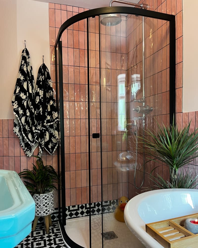 Glass shower with black frame in newly renovated bathroom with pink tile.