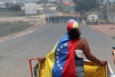 A woman looks at Venezuelan national guard members, at the border, seen from in Pacaraima, Brazil February 24, 2019. REUTERS/Ricardo Moraes