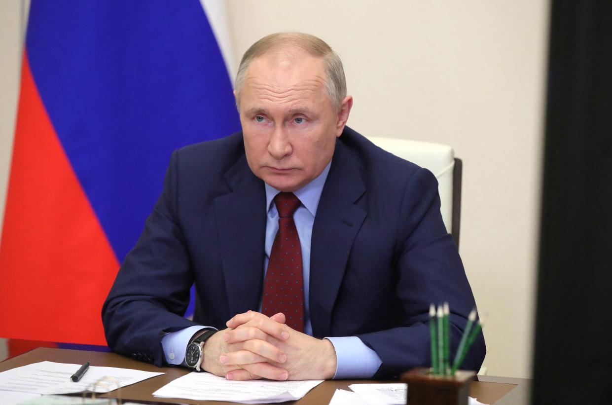 President Vladimir Putin, hands clasped, at a conference table, with pencils and a pen at his side.