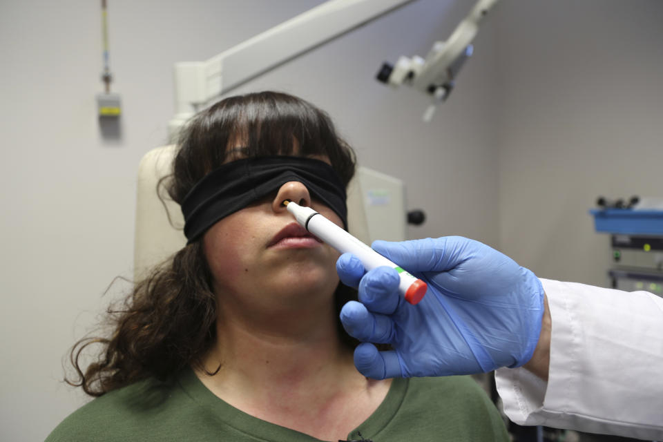 The hand of Dr. Clair Vandersteen wafts a tube of odors under the nose of a blindfolded patient, Gabriella Forgione, during tests in a hospital in Nice, southern France, Monday, Feb. 8, 2021, to help determine why she has been unable to smell or taste since she contracted COVID-19 in November 2020. A year into the coronavirus pandemic, doctors and researchers are still striving to better understand and treat the accompanying epidemic of COVID-19-related anosmia — loss of smell — draining much of the joy of life from an increasing number of sensorially frustrated longer-term sufferers like Forgione. (AP Photo/John Leicester)