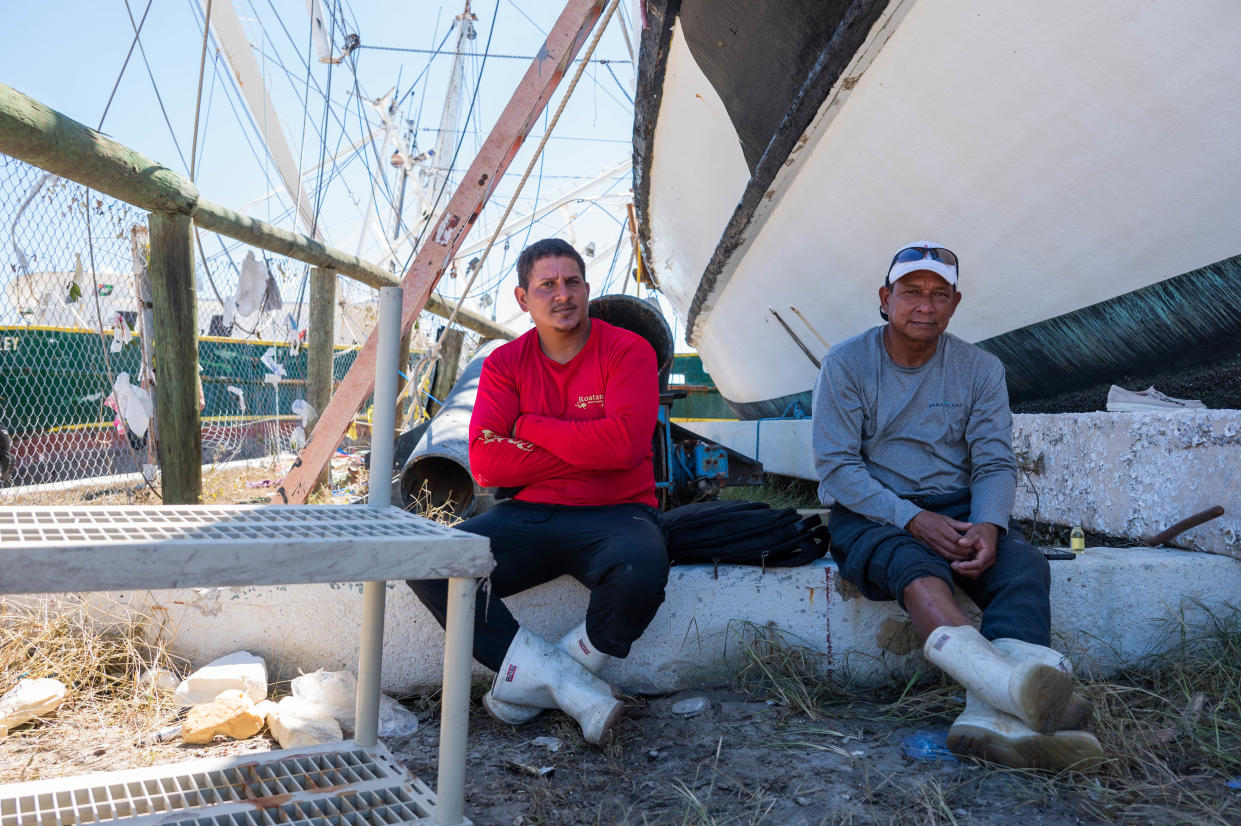 Shrimp boat workers Javier Allan Lopez, left, 34, and Oriel Martinez Alvarado, 51, sit in the shade of one of the shrimp boats that some of their fellow workers sought shelter in during Hurricane Ian near Trico Shrimp Co. in Fort Myers, Fla., on Friday. With nowhere else to go, Alvarado said the workers resorted to moving from boat to boat as the storm made each successive vessel increasingly perilous.